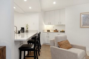 A modern kitchen with white cabinets, a dining area with black chairs, and a grey sofa with a brown pillow. - Fallridge Condo - Steps to Nordic Center & Bus (Vail)