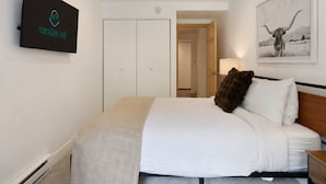 A bedroom with a bed, a TV mounted on the wall, a wardrobe, and a door leading to another room. - Fallridge Condo - Steps to Nordic Center & Bus (Vail)