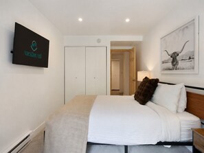 A bedroom with a bed, a TV mounted on the wall, a wardrobe, and a door leading to another room. - Fallridge Condo - Steps to Nordic Center & Bus (Vail)