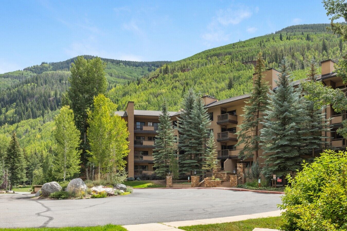 A multi-story hotel with a parking lot, surrounded by trees and mountains.