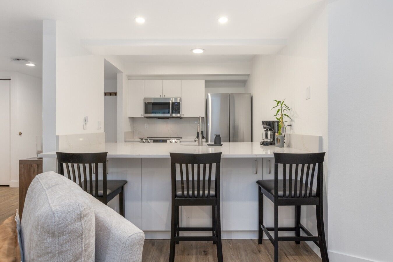 Una cocina moderna con armarios blancos, electrodomésticos de acero inoxidable y una isla central con dos taburetes de bar.