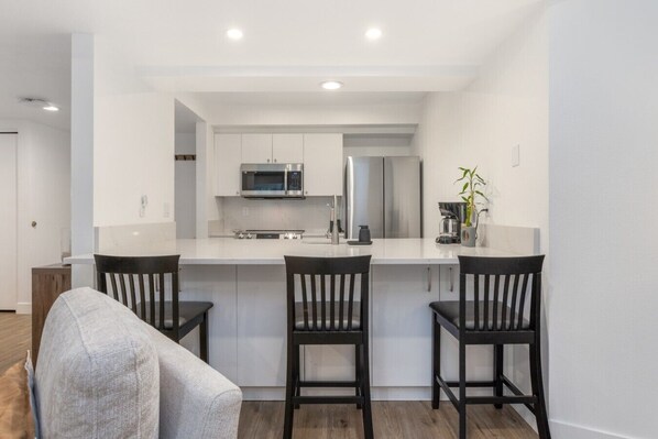 A modern kitchen with white cabinets, stainless steel appliances, and a central island with two bar stools. - Fallridge Condo - Steps to Nordic Center & Bus (Vail)