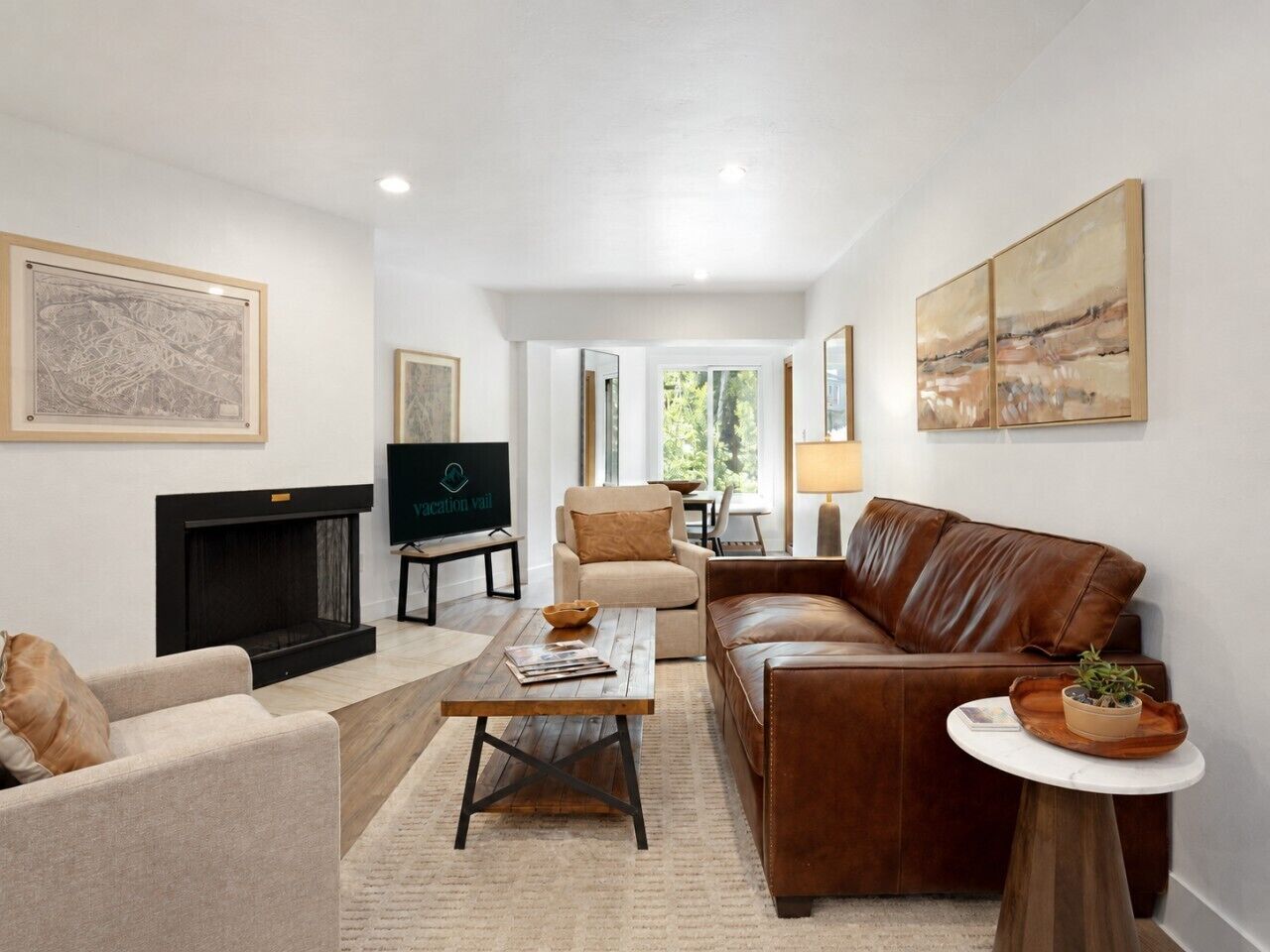 Un salon avec une cheminée, un canapé en cuir, des fauteuils, une table basse et des œuvres d’art accrochées aux murs.