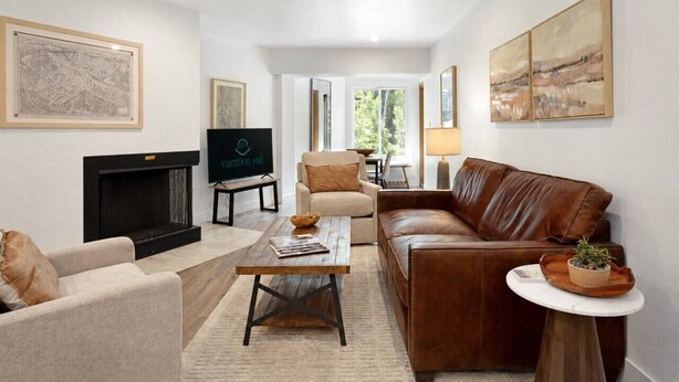 A living room with a fireplace, leather sofa, armchairs, a coffee table, and artwork on the walls. - Fallridge Condo - Steps to Nordic Center & Bus (Vail)