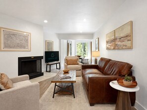 A living room with a fireplace, leather sofa, armchairs, a coffee table, and artwork on the walls. - Fallridge Condo - Steps to Nordic Center & Bus (Vail)