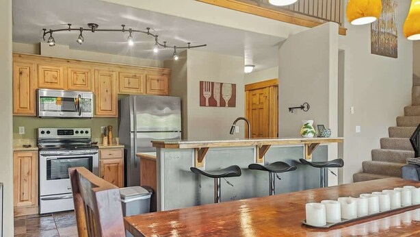 A kitchen with wooden cabinets, a stainless steel oven, a refrigerator, and a bar area with stools.