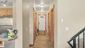 A hallway with a tiled floor, wooden doors, a white door at the end, and a staircase with a black railing.