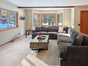 A living room with a sectional sofa, a coffee table, and large windows.