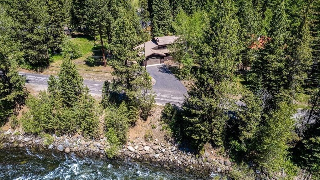A house surrounded by dense forest with a driveway leading to a gated entrance.