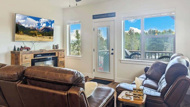 A living room with leather recliners, a television, and a scenic view through the windows. - McCall Summer Base | 3BR Townhome w/ Views & A/C (McCall)