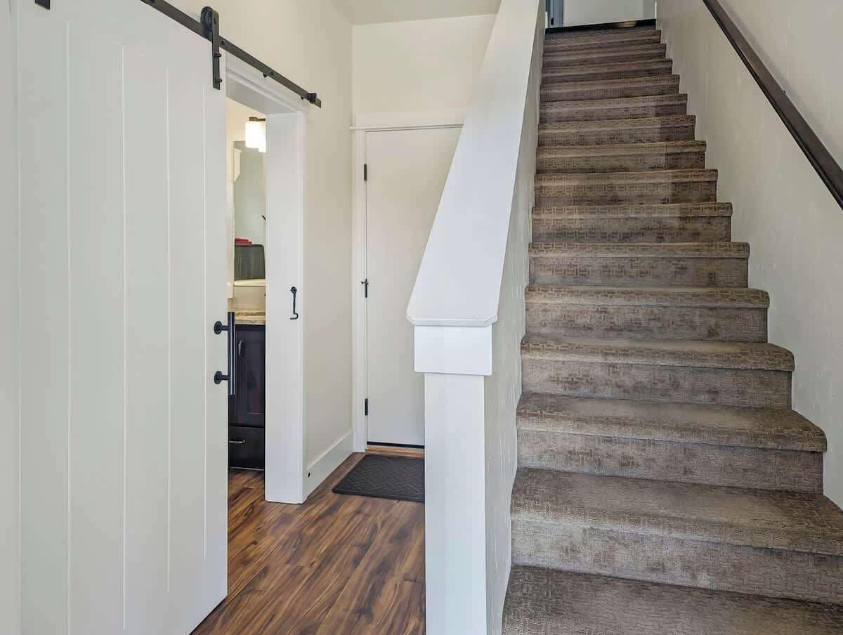 Una escalera de madera con barandilla blanca que conduce a una habitación con una puerta.