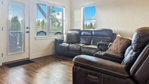 A living room with a sectional sofa, a door with a window, and a view of trees. - McCall Summer Base | 3BR Townhome w/ Views & A/C (McCall)