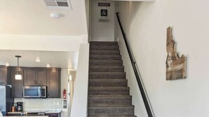 A staircase leading to a kitchen area with dark wood flooring, a modern kitchen with dark cabinets, and a hanging sign that reads "ALWAYS & Forever". - McCall Summer Base | 3BR Townhome w/ Views & A/C (McCall)