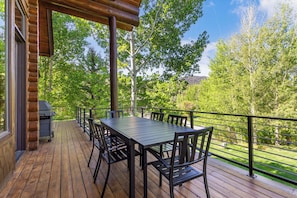 Une terrasse en bois avec une table et des chaises, un barbecue et une vue sur les arbres et un paysage lointain.