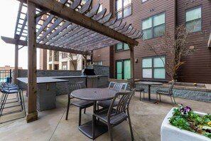 Un patio al aire libre con una parrilla, asientos y una pérgola.