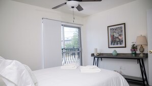 Ein Schlafzimmer mit Bett, Schreibtisch, Deckenventilator, Fenster und einem gerahmten Bild an der Wand.