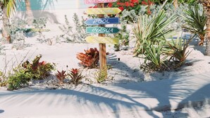 A wooden signpost with multiple directional signs pointing to various locations such as Beach, Bimini, Andros, Abaco, Eleuthera, Mayaguana, Exuma, Pool, and Inagua. - Oceanview Rooftop Townhouse Sunrise & Sunset Views (Roker's Point)