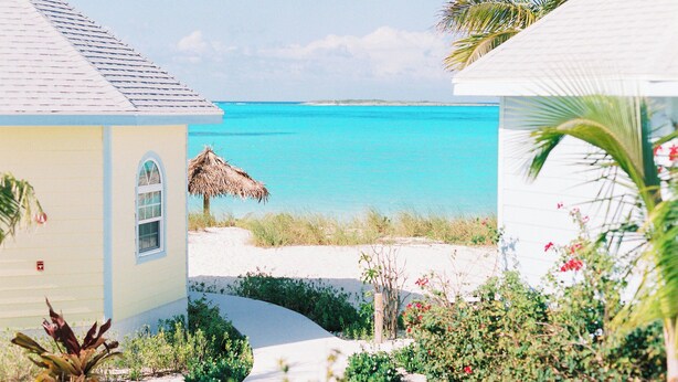 A beachfront property with a thatched-roof structure, a sandy pathway, and lush greenery. - Oceanview Rooftop Townhouse Sunrise & Sunset Views (Roker's Point)