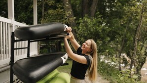 Une personne est en train de régler un appareil d’exercice noir et vert sur une véranda.