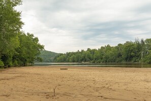 A sandy beach with a log, trees, and a lake.