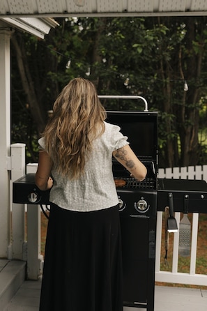 A person grilling outdoors with a barbecue grill and a white fence in the background. - Waterfront | 15 min Tremblant • HotTub • Fireplace (Les Laurentides Regional County Municipality)