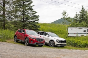 Two cars parked on a gravel road with a trailer in the background. - Waterfront | 15 min Tremblant • HotTub • Fireplace (Les Laurentides Regional County Municipality)