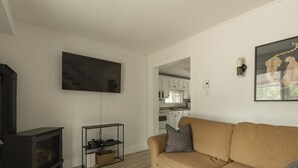 Un salon avec un canapé, un téléviseur, une cheminée et une cuisine en arrière-plan.