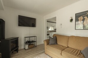 A living room with a sofa, a TV, a fireplace, and a kitchen in the background.