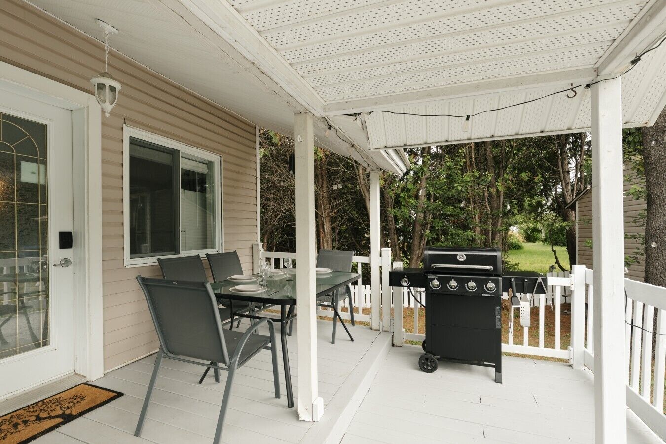 Een overdekt terras met een barbecue, eettafel en stoelen.