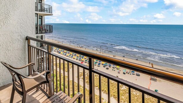 A balcony with a view of the beach, a railing, and two wooden chairs. - The Caribbean Resort and Villa 1221 (Myrtle beach)