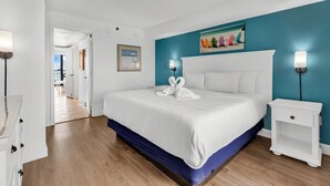 A bedroom with a bed, a nightstand, a painting, and a hallway leading to another room. - The Caribbean Resort and Villa 1221 (Myrtle beach)