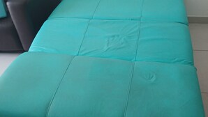 Ein blaugrünes, bezogenes Sofa in einem Raum mit gefliestem Boden und einer schlichten weißen Wand.