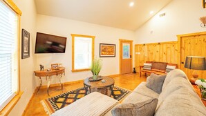 A cozy living room with a sofa, a coffee table, and a TV mounted on the wall.