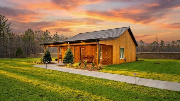 A wooden cabin with a covered porch, a small Christmas tree, and a well-maintained lawn.