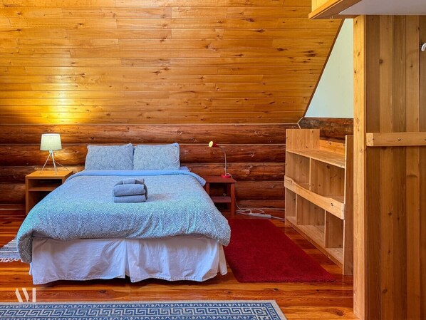 A wooden cabin bedroom with a bed, nightstands, a red rug, and a built-in wooden shelf. - Raven`s Roost - Rural Cabin Minutes from Golden (Golden)