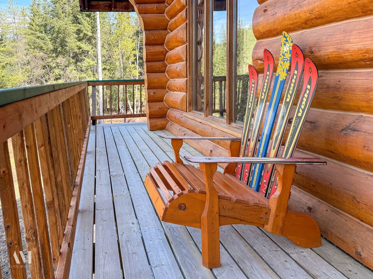 A wooden deck with a bench and skis leaning against a log cabin wall.