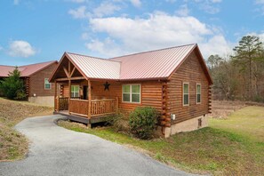 A log cabin with a porch, a metal roof, and a small garden area. - 2BR Retreat - Hot Tub, Near Dollywood & Pkwy! (Pigeon Forge)