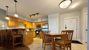 A modern kitchen with wooden cabinets, a dining area with a table and chairs, and a microwave.