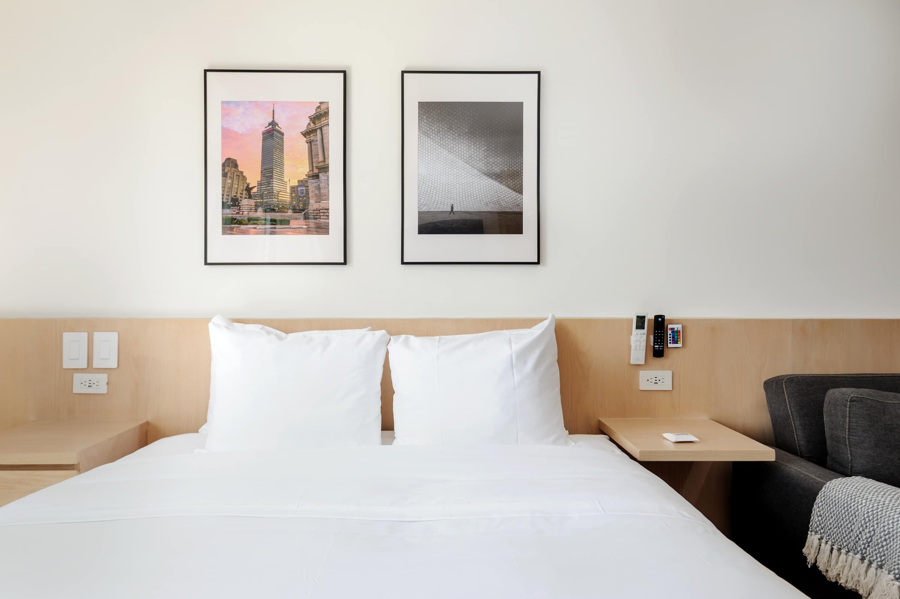 Une chambre d’hôtel avec un lit, deux tableaux encadrés au mur, une table de chevet, une télécommande et une chaise.