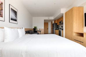 Ein modernes Hotelzimmer mit einem großen Bett, einem kleinen Schreibtisch, einem Sessel, einem Fernseher und einer Küchenzeile.