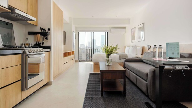 Een moderne keuken met een ingebouwde oven en kookplaat, een zithoek met een bank en salontafel, en een balkon met uitzicht op de stad.