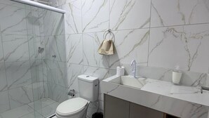 Un bagno moderno con cabina doccia in vetro, un WC, un lavabo con specchio e un asciugamano appeso al muro.