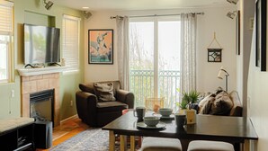 A cozy living room with a fireplace, a sofa, a dining table with stools, and a TV mounted on the wall. - Cozy 2-bedroom townhome in OB with sunny deck and AC (San Diego)