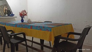 Un coin repas avec une table recouverte d’une nappe colorée, entourée de chaises noires. Un vase rempli de fleurs est posé sur la table.