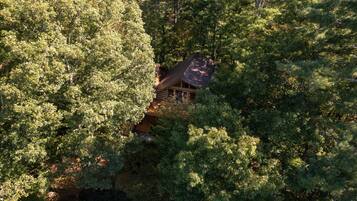 Une cabane nichée au milieu d’une forêt dense, dotée d’une terrasse en bois visible et d’un toit en pente.