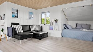 A modern bedroom with a bed, a black leather sofa, and a window with a view of greenery.