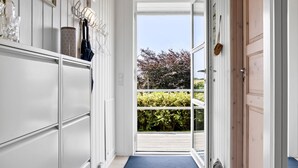 A hallway with white cabinetry, a blue mat at the entrance, and a view of greenery outside.