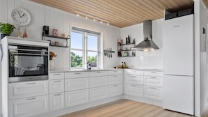 A modern kitchen with white cabinetry, a built-in oven, a stainless steel refrigerator, and a window providing natural light.