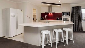 Una cucina moderna con isola centrale, sgabelli da bar bianchi, forno a microonde integrato e una parete di accentazione rossa.