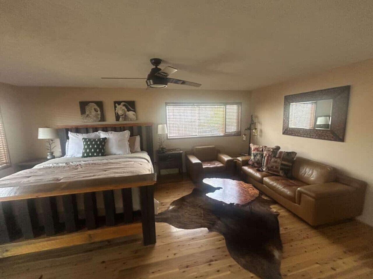 A bedroom with a wooden bed, a leather sofa, a coffee table, and a ceiling fan.